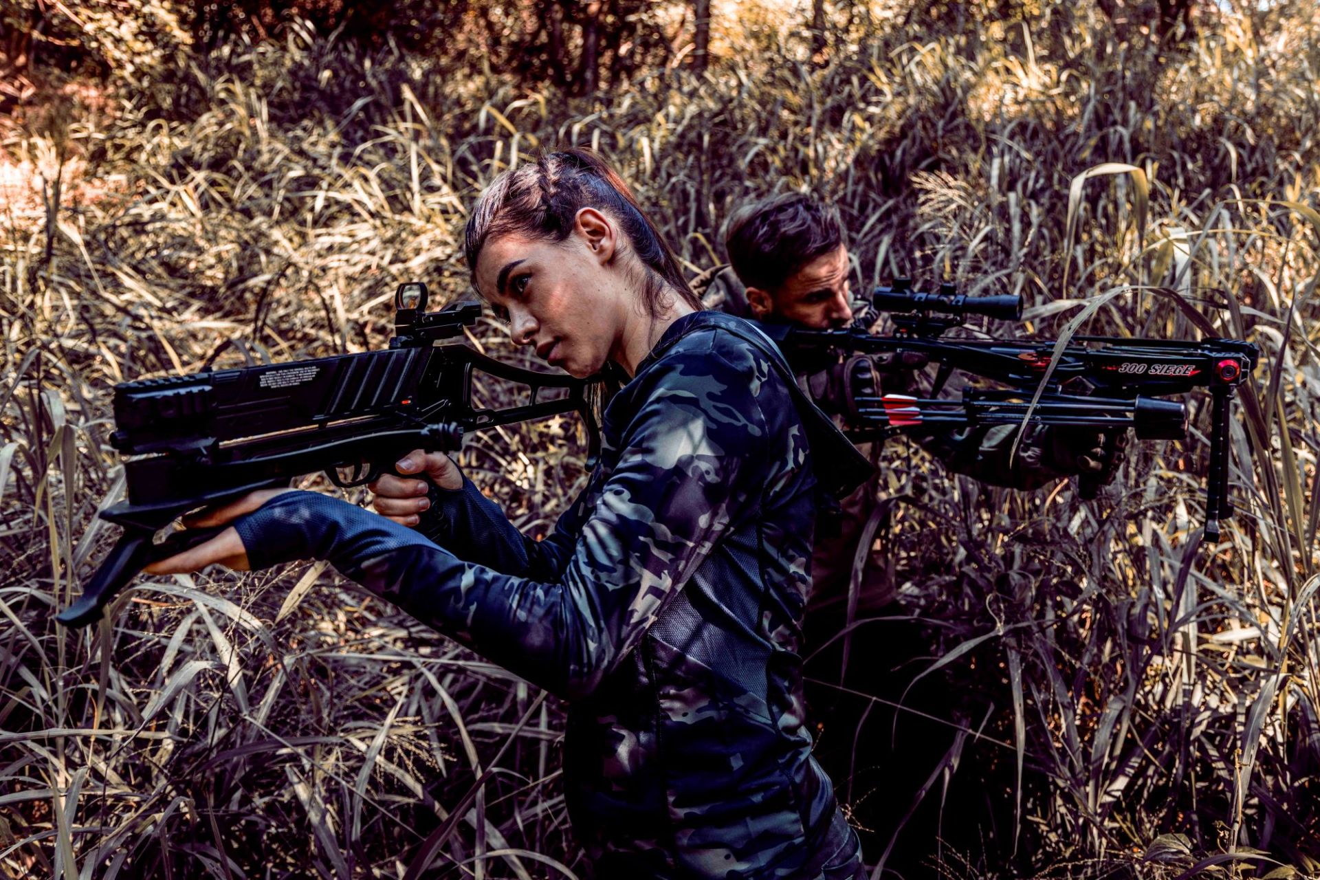 Two shooters aiming crossbows equipped with sights in tall grass